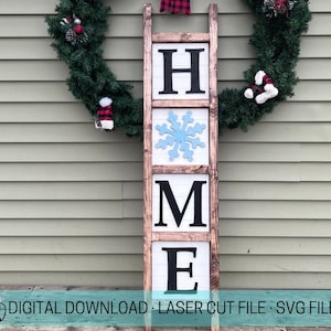 以下が含まれることがあります： 「HOME」という文字が各段に黒文字で書かれた木製のはしご。3段目に青い雪の結晶があります。はしごは緑色の壁に寄りかかり、クリスマスリースが飾られています。