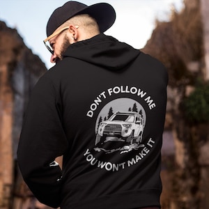 Op de afbeelding: Zwart hoodie met een witte grafische print van een auto die off-road rijdt. De grafiek bevat de tekst "Don't Follow Me You Won't Make It".