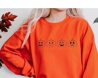 May include: Orange sweatshirt with a row of five black outlined pumpkins with different facial expressions. The pumpkins are all the same size and are evenly spaced.