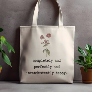 May include: A white canvas tote bag with a floral design and the text "completely and perfectly and incandescently happy."