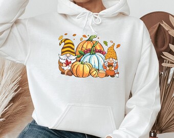 May include: White hoodie with a graphic of three gnomes holding pumpkins and a cup of coffee. The gnomes are wearing red, yellow, and brown hats. The pumpkins are orange and white.