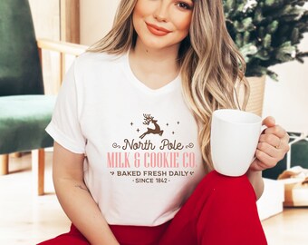 May include: White t-shirt with a brown reindeer graphic and the text "North Pole Milk & Cookie Co. Baked Fresh Daily - Since 1842."
