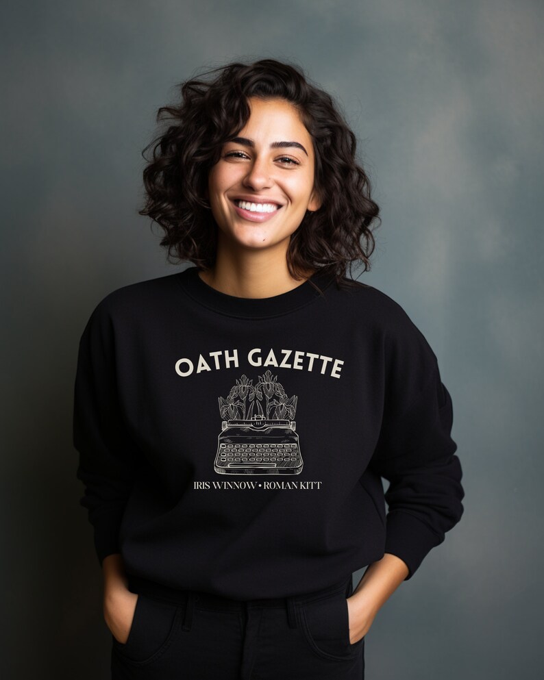 Puede incluir: Sudadera negra con un gr&aacute;fico blanco de una m&aacute;quina de escribir con flores y el texto "OATH GAZETTE IRIS WINNOW - ROMAN KITT"