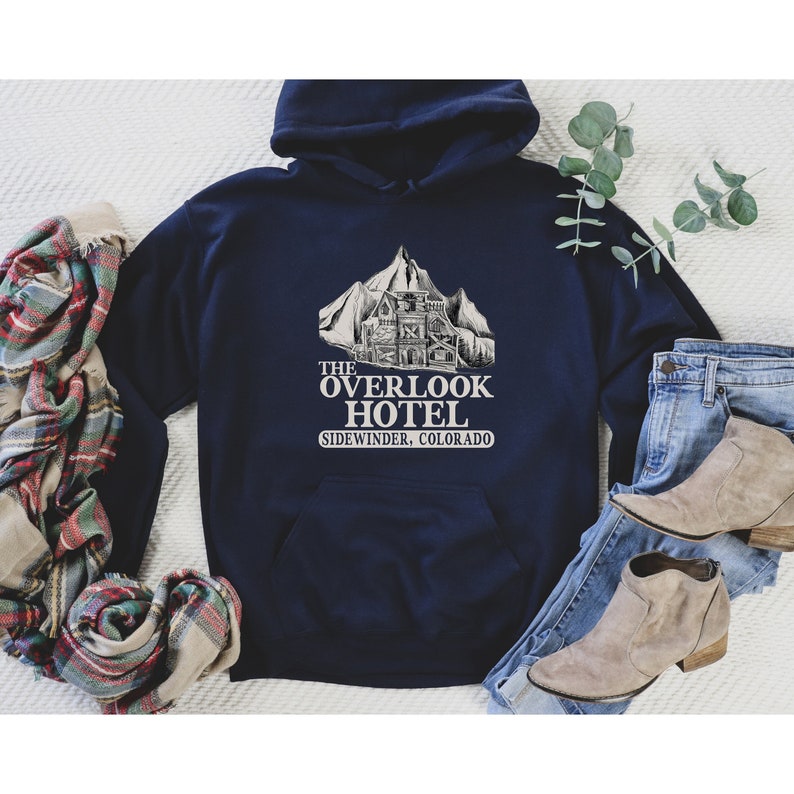 May include: A navy blue hoodie with a white graphic of a mountain range and a building with the text "THE OVERLOOK HOTEL SIDEWINDER, COLORADO".