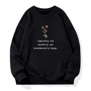 Puede incluir: Sudadera negra con un gr&aacute;fico floral y el texto "completely and perfectly and incandescently happy."