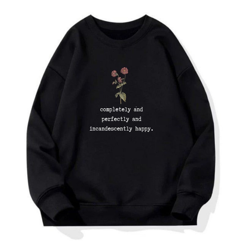 Puede incluir: Sudadera negra con un gr&aacute;fico floral y el texto "completely and perfectly and incandescently happy."