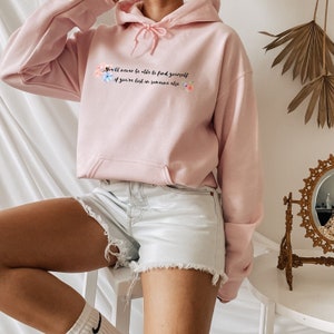 Peut inclure: Un sweat &agrave; capuche rose avec un motif floral et le texte "You'll never be able to find yourself if you're lost in someone else".