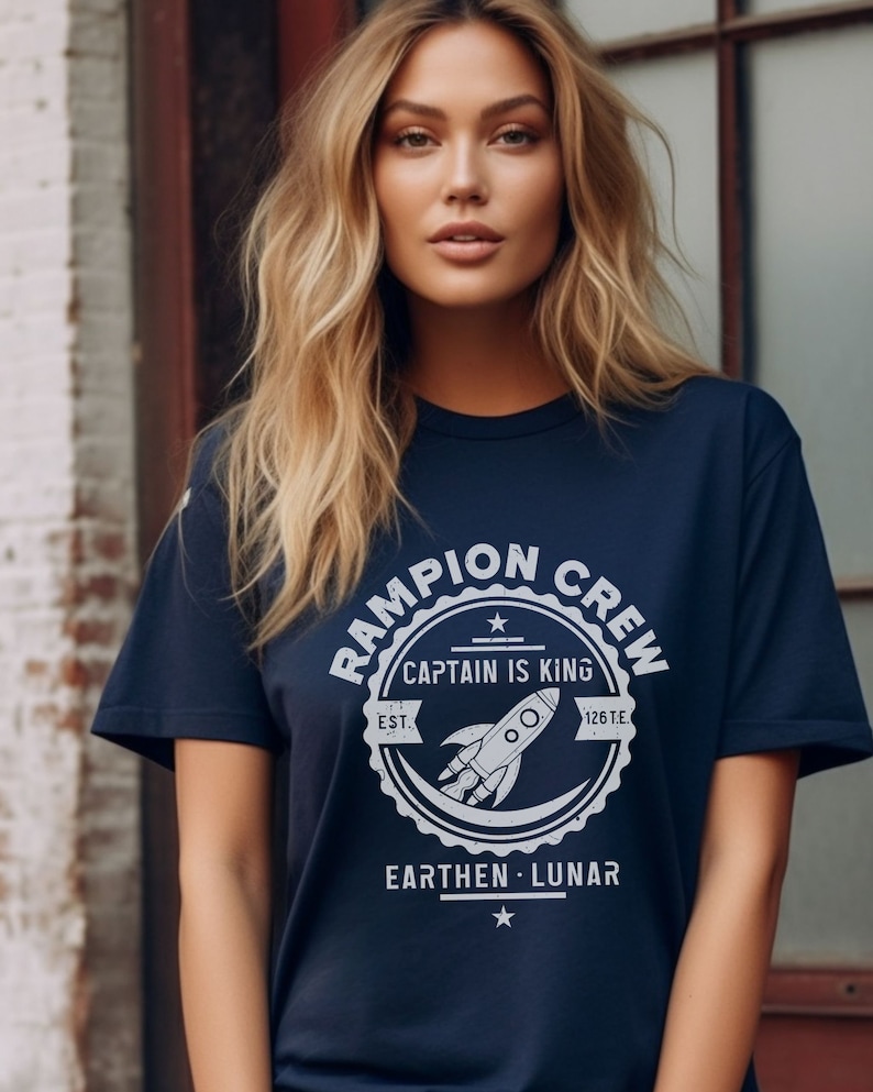 May include: A navy blue t-shirt with a white graphic of a rocket ship and the text "Rampion Crew, Captain is King, Est. 1267 E, Earthen - Lunar".