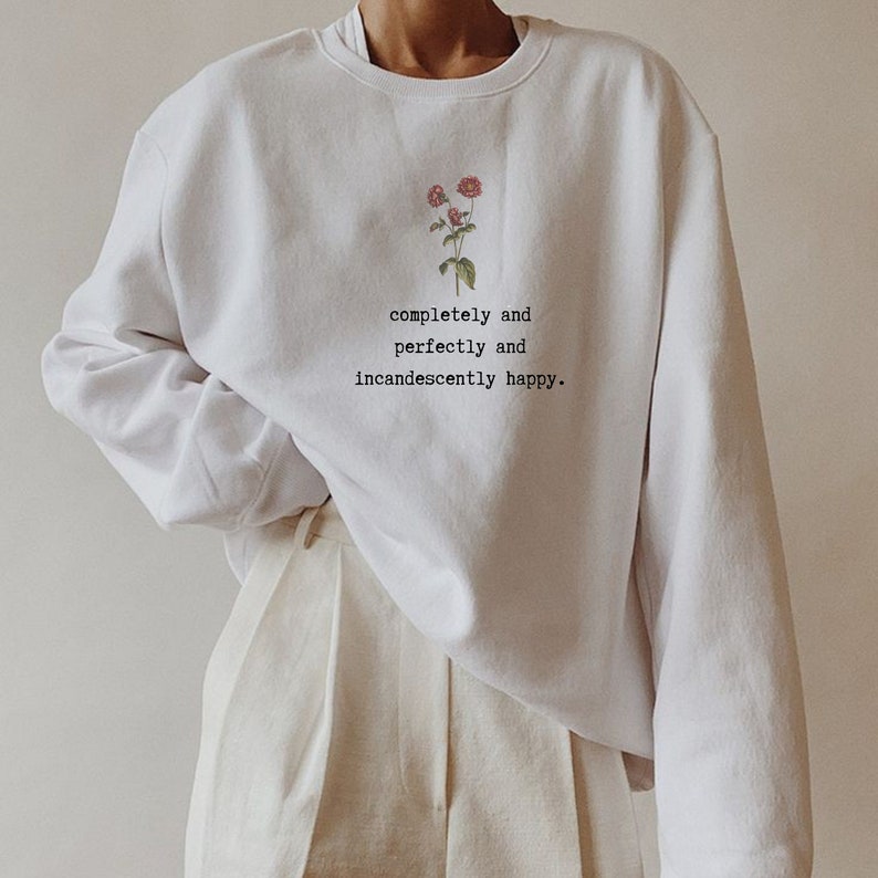 Puede incluir: Sudadera blanca con un dise&ntilde;o floral y el texto "completely and perfectly and incandescently happy."