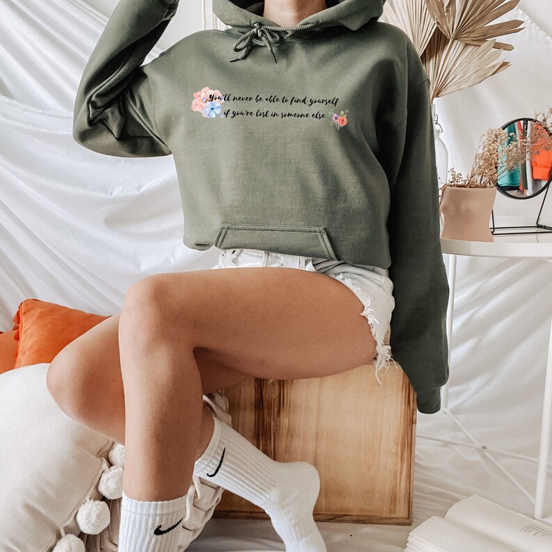 Peut inclure: Un sweat &agrave; capuche court de couleur vert avec un motif floral et le texte "You'll never be able to find yourself if you're lost in someone else."