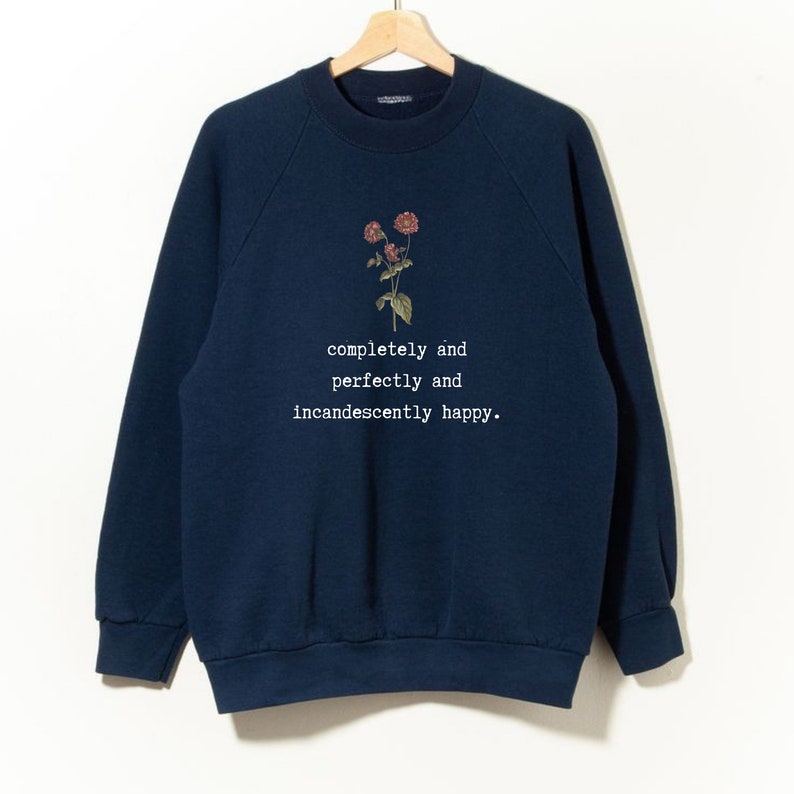 Puede incluir: Una sudadera azul marino con un gr&aacute;fico floral y el texto "completely and perfectly and incandescently happy."