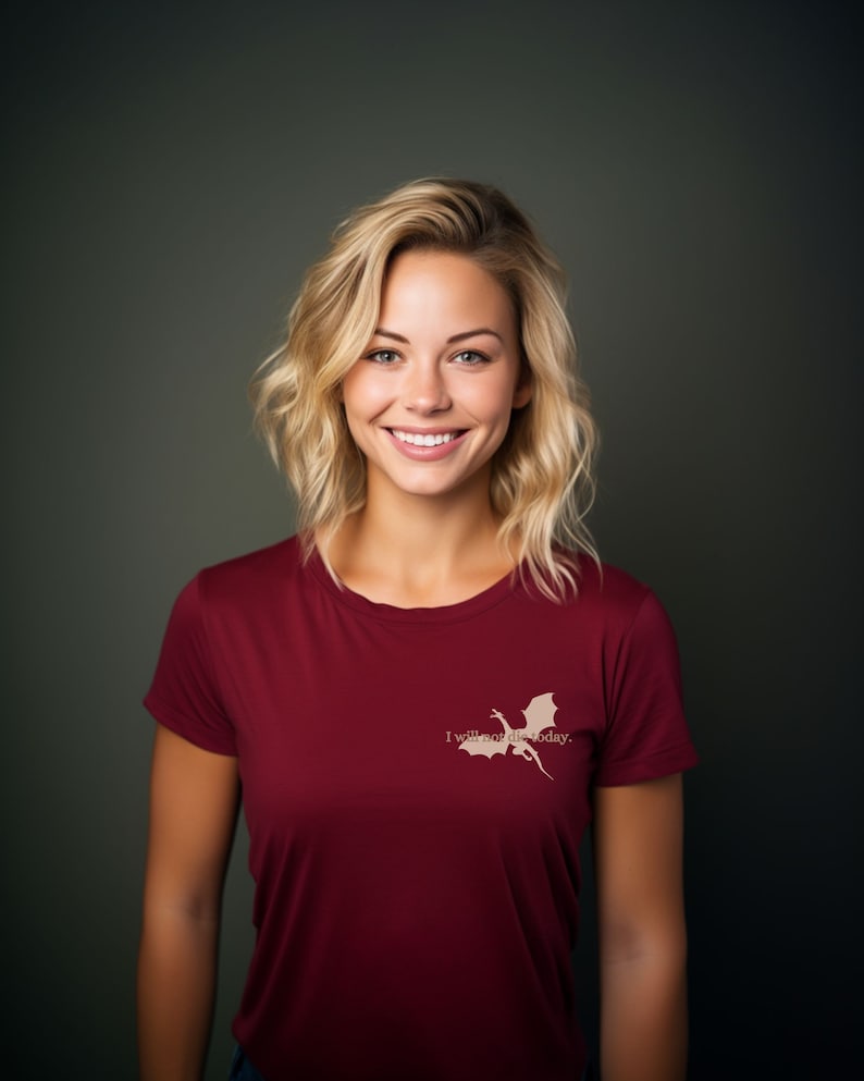May include: A woman with blonde hair is wearing a maroon t-shirt with a white dragon graphic and the text "I will not die today."