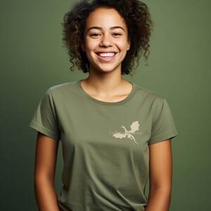 May include: A woman with curly brown hair is smiling and wearing a green t-shirt with a white dragon silhouette and the text "I will not die today."