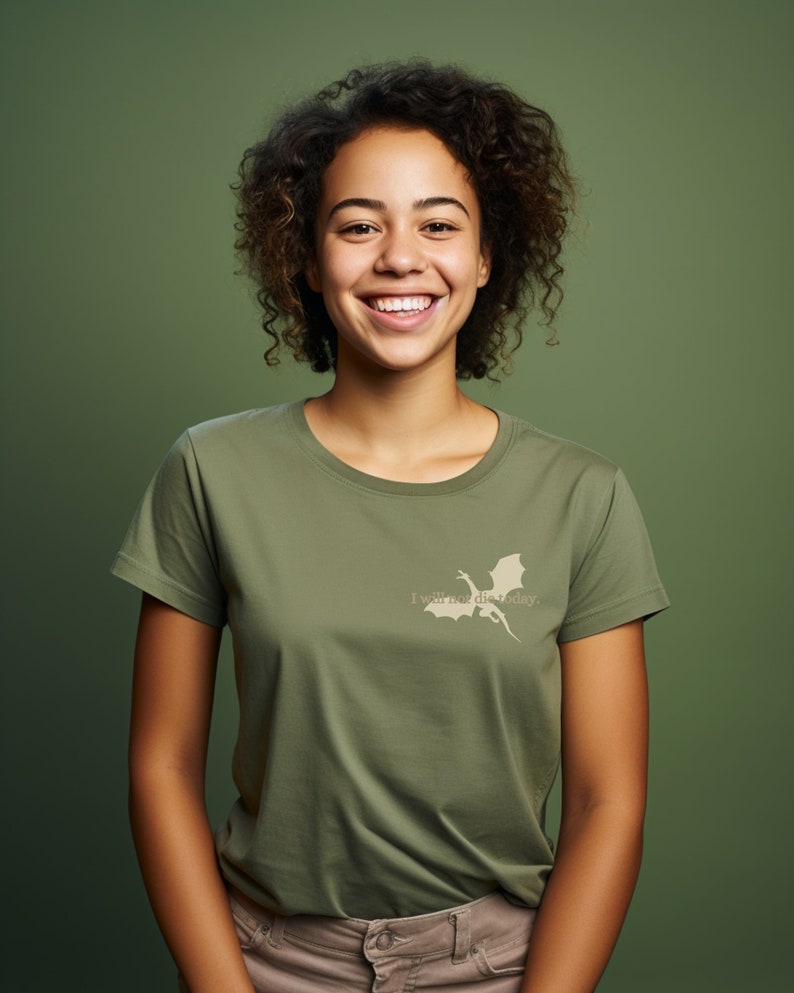 May include: A woman with curly brown hair is smiling and wearing a green t-shirt with a white dragon silhouette and the text "I will not die today."