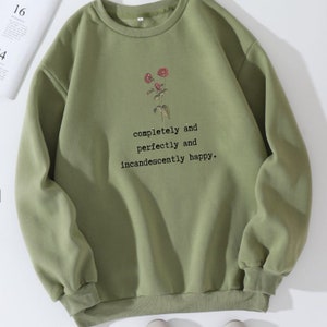 Puede incluir: Una sudadera verde con un dise&ntilde;o floral y el texto "completely and perfectly and incandescently happy."