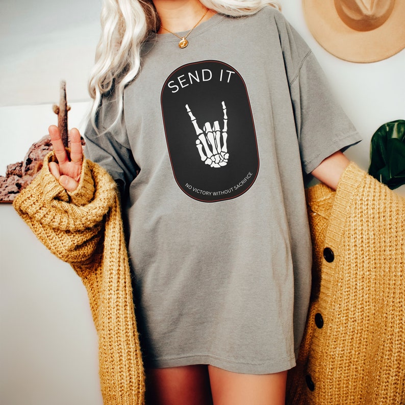 May include: Gray oversized t-shirt with a black oval graphic featuring a skeleton hand making the rock and roll sign. The text "SEND IT" is above the hand and "NO VICTORY WITHOUT SACRIFICE" is below the hand.