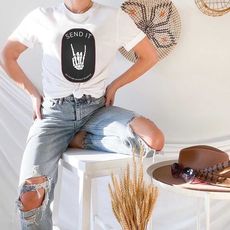 May include: White t-shirt with a black circle graphic featuring a skeleton hand making a rock and roll sign. The text "SEND IT" is above the graphic and "NO VICTORY WITHOUT SACRIFICE" is below the graphic.