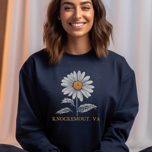 Puede incluir: Sudadera azul marino con un gr&aacute;fico de margarita blanca y el texto "Knockemout, VA".