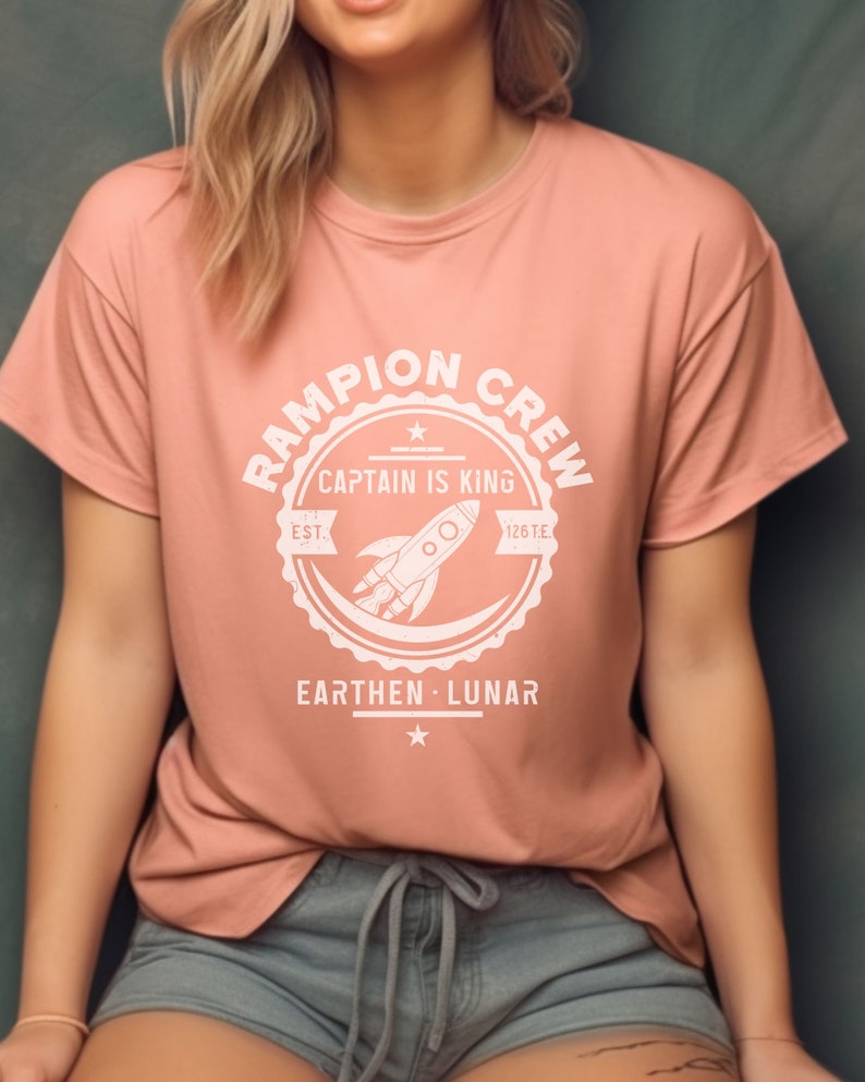 May include: A pink t-shirt with a white graphic of a rocket ship and the text "Rampion Crew, Captain is King, Est. 126 T.E., Earthen - Lunar".