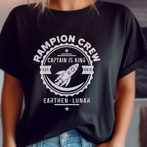 May include: Black t-shirt with a white graphic of a rocket ship and the text "Rampion Crew, Captain is King, Est. 126 T.E., Earthen - Lunar".