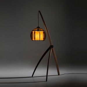 May include: A wooden floor lamp with a curved arm and a tripod base. The lampshade is made of wood and has a warm, yellow glow.