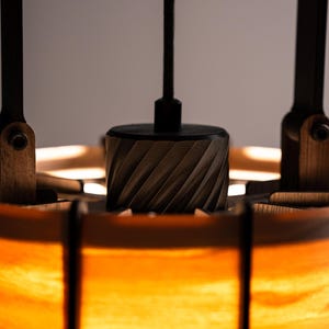 Pu&ograve; includere: Primo piano di un lampadario in legno. Il lampadario ha un centro cilindrico con un design intagliato, sostenuto da bracci in legno e un paralume caldo e luminoso. Il design incorpora toni di legno naturale e una luce calda.