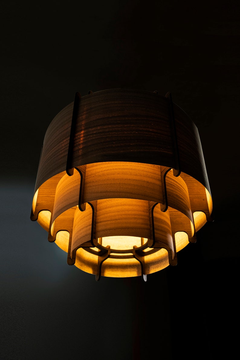 May include: A wooden pendant light fixture with a layered design. The light fixture is made of multiple layers of wood, each with a different shape. The light fixture is lit and casts a warm glow.