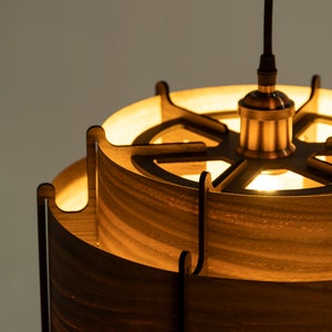 May include: A wooden pendant light with a circular, openwork design. The light is made of multiple layers of wood, creating a layered effect. The light is illuminated, casting a warm glow.