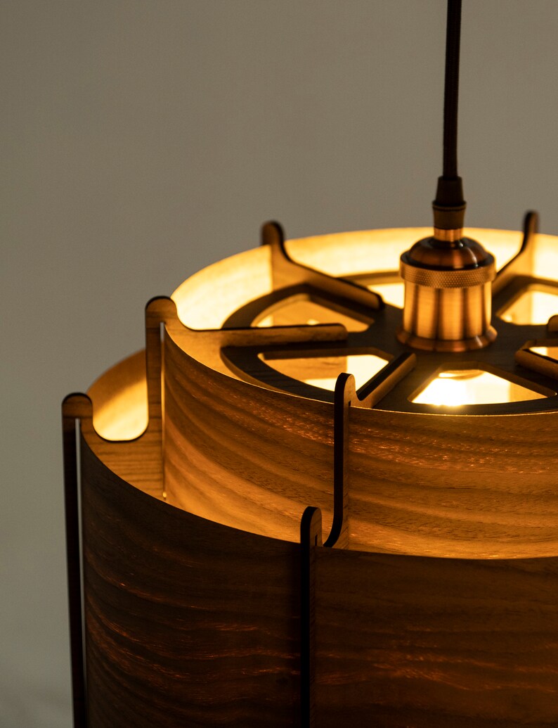 May include: A wooden pendant light with a circular, openwork design. The light is made of multiple layers of wood, creating a layered effect. The light is illuminated, casting a warm glow.