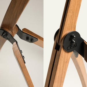 Pu&ograve; includere: Primo piano di una lampada a treppiede in legno con cerniere e dettagli in metallo nero. Le gambe in legno della lampada sono marrone chiaro e curve, collegate da piastre metalliche nere. La parola "CREAL" &egrave; visibile.