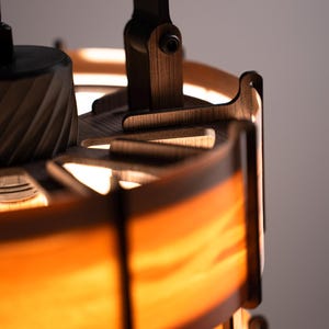 Pu&ograve; includere: Primo piano di una lampada in legno con una calda luce arancione. La lampada presenta un design a strati con dettagli in legno marrone scuro e un braccio orientabile. Il design &egrave; moderno e minimalista, adatto all'arredamento.