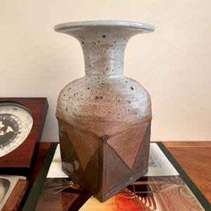以下が含まれることがあります： 茶色、白、グレーの斑点模様の釉薬が施された陶器の花瓶。花瓶は四角い底と広がった上部を持っています。