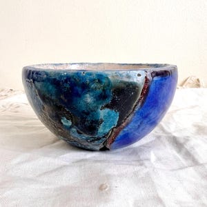 Könnte beinhalten: Eine handgefertigte Keramikschale mit einem einzigartigen, abstrakten Design. Die Schale zeigt eine Mischung aus Blautönen, darunter tiefes Marineblau, Türkis und hellere Farbtöne, mit Akzenten in Braun und Schwarz. Die Außenseite der Schale hat ein glänzendes Finish.
