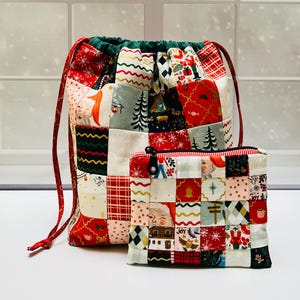 May include: A patchwork drawstring bag and a matching zippered pouch made from fabric featuring Christmas-themed illustrations including Santa Claus, pine trees, snowflakes, and the word JOY in red, green, white, and gold colors.