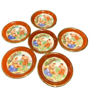 May include: Set of six orange and gold ceramic coasters featuring a painted design of people in a garden setting.