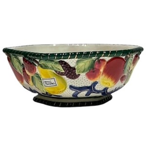May include: A large oval ceramic bowl with a white background and a colourful fruit design. The bowl has a green rim and a black base. The fruit design includes pears, apples, strawberries, and grapes.
