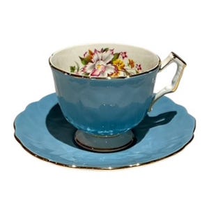 May include: A blue teacup and saucer set with a floral design. The cup has a white interior and a gold rim. The saucer has a scalloped edge and a gold rim.