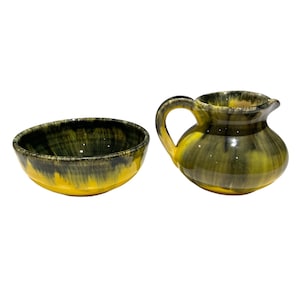 May include: A yellow and black ceramic creamer and sugar bowl set. The creamer has a handle and a rounded body. The sugar bowl is round and has a wide rim.