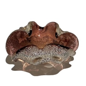 Peut inclure: Un cendrier décoratif de forme organique unique. Le cendrier présente un mélange de couleurs, notamment des nuances de rose, de marron et d'argent. Le verre a un aspect texturé, avec un motif moucheté sur la partie inférieure. Le design est élégant et artistique.