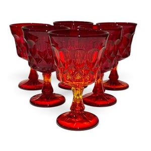 Peut inclure: Un ensemble de six verres à pied en verre rouge rubis disposés en triangle. Chaque verre présente un motif en losange texturé sur le calice, une tige courte et une base circulaire. Le verre est translucide, laissant passer la lumière rouge.
