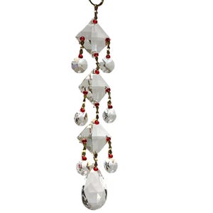 May include: A vertical hanging ornament featuring three clear faceted diamond-shaped crystals and one teardrop-shaped crystal at the base. The crystals are connected by thin gold-toned metal chains accented with small, round, vibrant red beads.