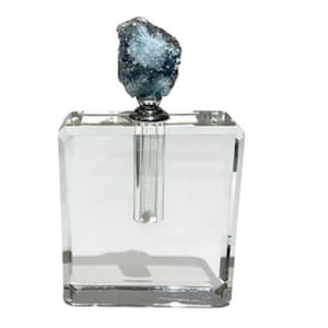 May include: A clear, square glass vase with a single, long, cylindrical opening. The vase is topped with a dark blue, textured crystal. The crystal is mounted on a silver-coloured metal base. The vase is designed for a single stem flower.