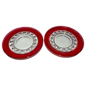 May include: Two red glass plates with a clear glass centre. The centre of the plates have a raised, scalloped design.