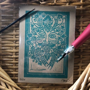 May include: A green and white woodblock print of the Green Man, a mythical figure with a face made of leaves and branches. The print is framed in a teal border and signed "Alison" in the bottom right corner. The print is numbered "3/20" in the bottom left corner.