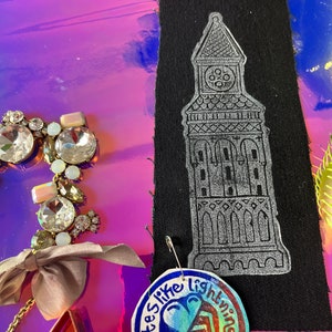 Peut inclure: Une collection de bijoux et d'accessoires faits à la main. Comprend un motif de tour argentée sur tissu noir, un charme rond avec le texte "tastes like lightning" et un collier de strass avec un nœud.