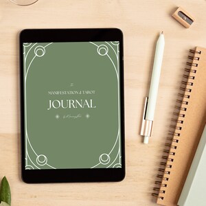 Könnte beinhalten: Ein digitales Tablet zeigt einen grünen Bildschirm mit dem Text "MANIFESTATION & TAROT JOURNAL". Ein Stift, Notizbücher, Bleistifte und eine Brille sind auf einer hellen Holzoberfläche darum angeordnet. Ein Zweig mit grünen Blättern befindet sich links.