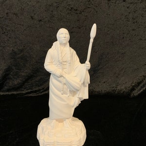 May include: White ceramic figurine of a Native American man holding a spear, wearing traditional clothing and standing on a textured base.