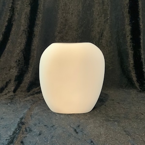 May include: A cream-colored, rounded vase with a wide opening. The vase has a smooth, matte finish and a simple, modern design. The vase is likely ceramic or porcelain and is suitable for displaying flowers or as a decorative accent.
