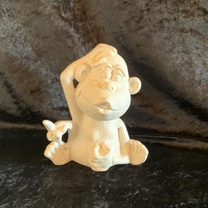 May include: A white ceramic figurine of a monkey with a thoughtful expression, holding a banana in one hand and a small cup in the other.