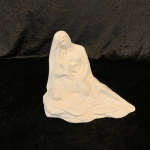 May include: White ceramic figurine of a Native American woman holding a fawn in her arms. The woman is sitting on a rock and has long flowing hair. The fawn is looking up at the woman.